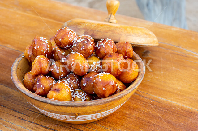 وصفات وأطباق الحلويات والسكريات، ضيافة المناسبات والأعياد العربية، طبق خشبي من اللقيمات ذهبية اللون، حلا الزلابيات الشرقي المغموسة بدبس التمر، كرات العجين المقلية الصغيرة المرشوشة بالسمسم، الحلوى الشهية واللذيذة