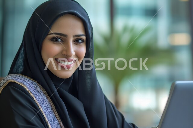 Completing work tasks remotely via the Internet, using modern and advanced technology, making video calls via the laptop, a close-up photo of a Saudi Arabian Gulf woman working on the laptop with happy gestures, female office professions and jobs