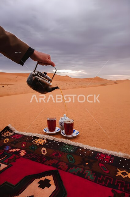 أماكن رحلات السفاري الترفيهية وسط الصحراء, رحلة و كشتة برية في المناطق الصحراوية، يد شخص يقوم بصب الشاي العربي التقليدي، الاستجمام والاستمتاع في الأجواء الهادئة, قضاء إجازة ممتعة في براري المملكة العربية السعودية