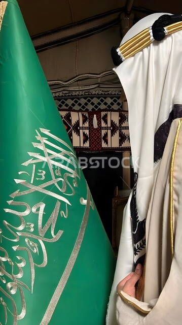 يوم العلم 11 مارس, الاحتفال بالمناسبات و الأعياد الوطنية, استذكار اليوم الوطني السعودي في 23 سبتمبر، الفخر و الاعتزاز بالهوية السعودية, مفهوم الحب و الانتماء للوطن, رجل عربي خليجي سعودي يرتدي الثوب التقليدي و الشماغ يقف بجانب علم المملكة العربية السعودية