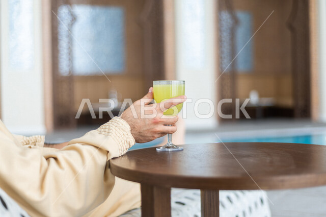 شاب عربي سعودي، الجلوس والاسترخاء في المسبح، شرب كاسة من عصير الليمون بعد السباحة