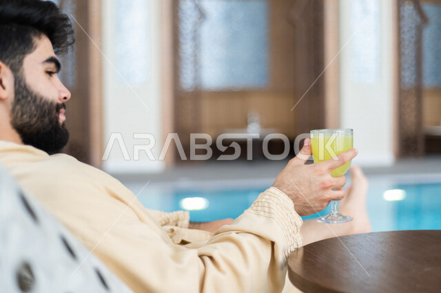 شاب عربي سعودي، الجلوس والاسترخاء في المسبح، شرب كاسة من عصير الليمون بعد السباحة