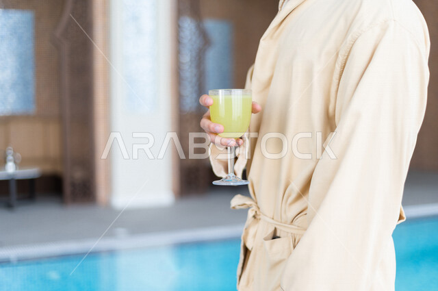شاب عربي سعودي، يحمل كاسة من عصير الليمون، الذهاب للجلوس والاسترخاء بعد السباحة