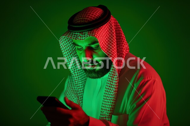 Using modern and advanced devices and technologies, close-up portrait of a Saudi Arabian Gulf man wearing traditional thobe and shemagh holding a mobile phone in his hand, communicating and chatting with friends, browsing social networking sites, green background