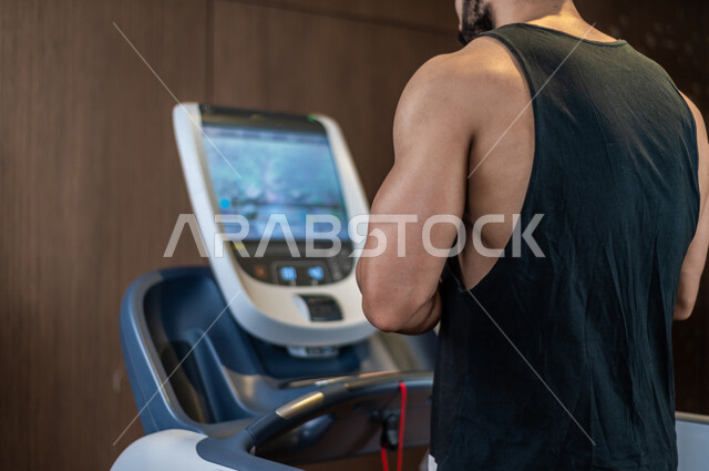 شاب عربي سعودي، يرتدي ملابس رياضية، التمرن والاحماء على جهاز المشي، صالة الألعاب الرياضية، تمارين قلب مكثفة، ممارسة الرياضة، اللياقة البدنية