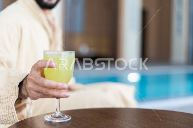 شاب عربي سعودي، الجلوس والاسترخاء في المسبح، شرب كاسة من عصير الليمون بعد السباحة