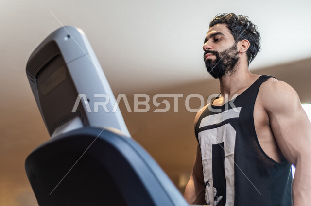 شاب عربي سعودي، يرتدي ملابس رياضية، التمرن والاحماء على جهاز المشي، صالة الألعاب الرياضية، تمارين قلب مكثفة، ممارسة الرياضة، اللياقة البدنية