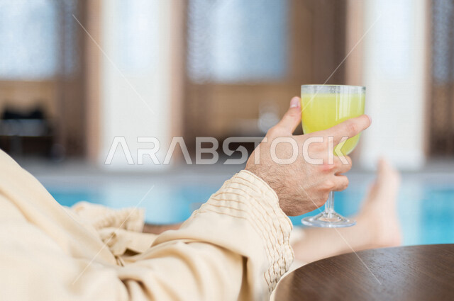 شاب عربي سعودي، الجلوس والاسترخاء في المسبح، شرب كاسة من عصير الليمون بعد السباحة