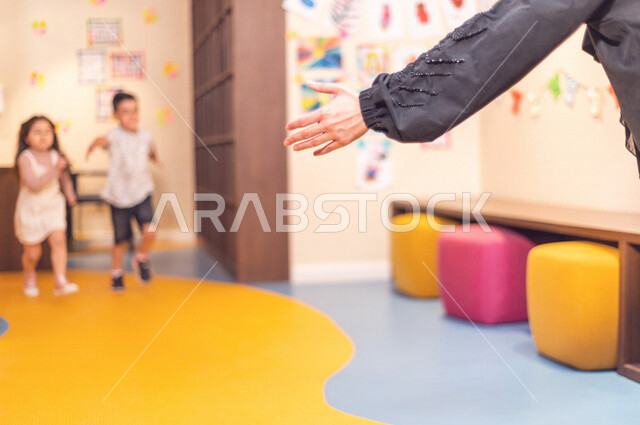 صورة مقربة لمعلمة عربية خليجية سعودية تستقبل بحفاوة طفلان عربيان خليجيان سعوديان ، حب و فرح ، آمان و طمأنينة ، حضانة أطفال ، روضة أطفال .