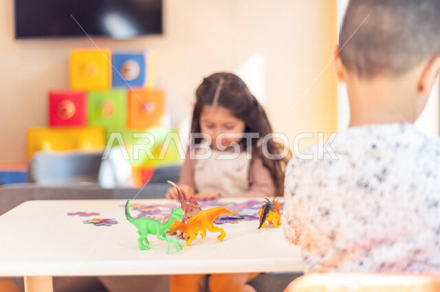 صورة لطفلة عربية خليجية سعودية تبدع بنشاط تركيب البازل ، و طفل عربي خليجي سعودي يلعب بالديناصورات ، ألعاب ترفيهية ، تعليم و ابداع ، تنمية مهارات ، حضانة أطفال ، روضة أطفال .