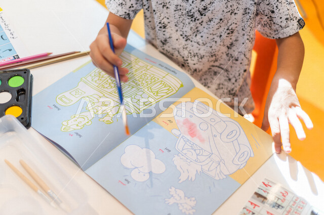 تصوير مقرب لدفتر رسومات التلوين ، طفل عربي خليجي سعودي يبدع بنشاط تلوين الرسومات ، أنشطة فنية و ترفيهية ، تعليم و ابداع ، تنمية مهارات ، حضانة أطفال ، روضة أطفال .