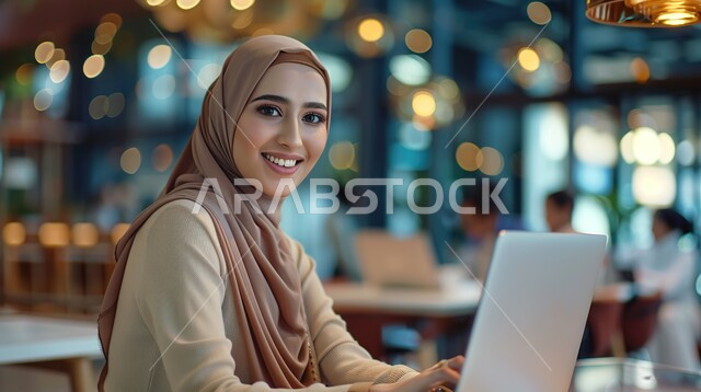 Integrating modern technologies into daily life, looking at the camera with gestures of happiness and pleasure, a smiling veiled Saudi Arabian Gulf woman wearing a black abaya sitting at the table and working on a laptop