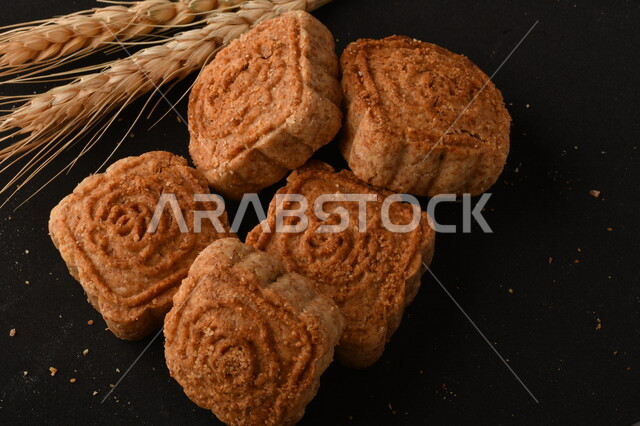 صورة مقربة لمعمول محشو مربع الشكل من الحلويات الشعبية الهشة اللذيذة على خلفية سوداء ، صورة لكعك بعجوة وبعرف بإسم كعك العيد الشهي ، خلفية سوداء لحلويات شعبية طازجة