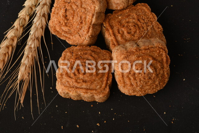 صورة مقربة لمعمول محشو مربع الشكل من الحلويات الشعبية الهشة اللذيذة على خلفية سوداء ، صورة لكعك بعجوة وبعرف بإسم كعك العيد الشهي ، خلفية سوداء لحلويات شعبية طازجة