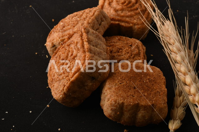 صورة مقربة لمعمول محشو مربع الشكل من الحلويات الشعبية الهشة اللذيذة على خلفية سوداء ، صورة لكعك بعجوة وبعرف بإسم كعك العيد الشهي ، خلفية سوداء لحلويات شعبية طازجة