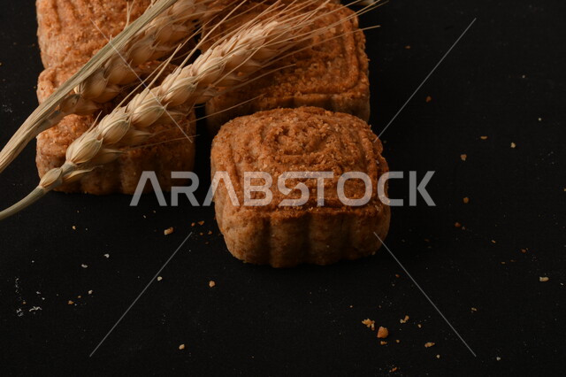 Close-up of a square-shaped stuffed Maamoul, a delicious, crunchy, popular sweet, on a black background, a picture of a date cookie, also known as a delicious Eid cookie, a black background of fresh, popular sweets