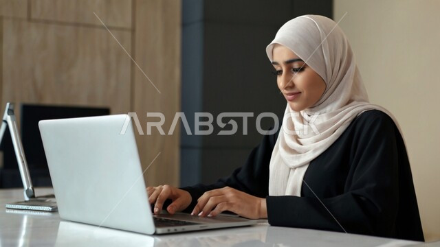 Using modern and advanced technological devices, office administrative professions and jobs, managing and organizing business affairs, a close-up image of a veiled Saudi Arabian Gulf female employee working on a computer inside the office, companies and offices of the Kingdom of Saudi Arabia