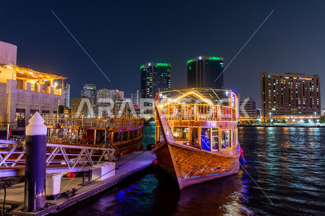 منظر انعكاس الأضواء على مياه البحر, مناطق جذب السياح من أنحاء العالم, قارب خشبي مضاء لنقل السائحين مضاء في مدينة دبي, جولات سياحية بحرية ممتعة في وقت الليل, أماكن السياحة الساحلية في الإمارات العربية المتحدة