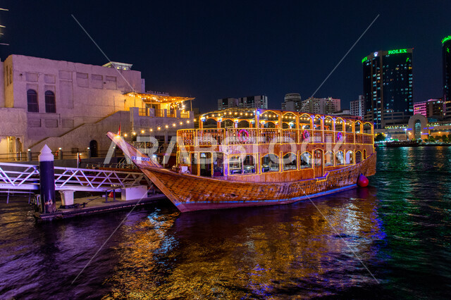 منظر انعكاس الأضواء على مياه البحر, مناطق جذب السياح من أنحاء العالم, قارب خشبي مضاء لنقل السائحين مضاء في مدينة دبي, جولات سياحية بحرية ممتعة في وقت الليل, أماكن السياحة الساحلية في الإمارات العربية المتحدة