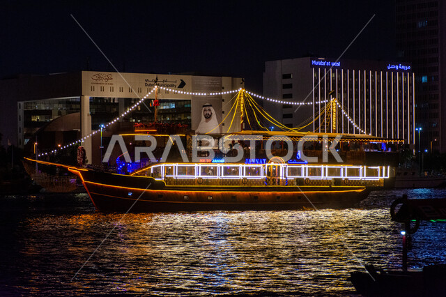 منظر انعكاس الأضواء على مياه البحر, مناطق جذب السياح من أنحاء العالم, قارب خشبي مضاء لنقل السائحين مضاء في مدينة دبي, جولات سياحية بحرية ممتعة في وقت الليل, أماكن السياحة الساحلية في الإمارات العربية المتحدة
