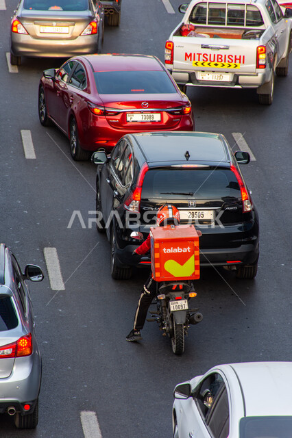 ازدحام السيارات في الطريق بمدينة دبي، مندوب يقود دراجة نارية لتوصيل الأكل من طلبات، وقت الذروة في الإمارات العربية المتحدة، خدمات الشحن ذات الجوة العالية, وسائل النقل و المواصلات البرية