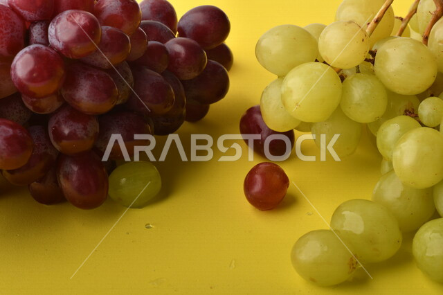 صورة لفاكهة العنب الأرجواني والأخضر اللذيذ على خلفية صفراء ، فاكهة العنب الصحية اللذيذة تظهر على شكل عناقيد ، فاكهة صيفية