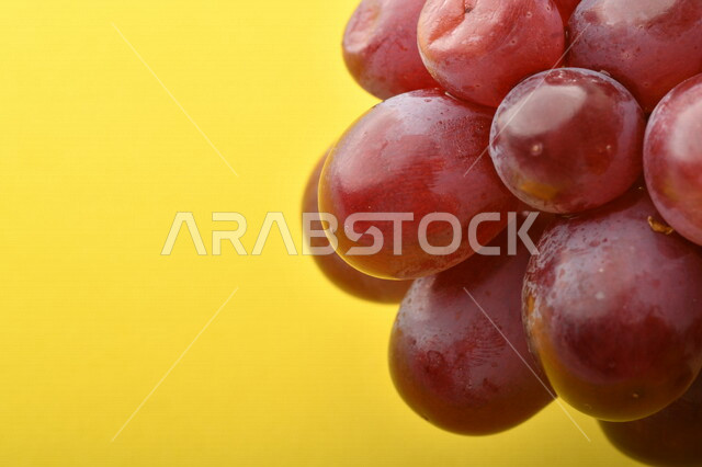 صورة لفاكهة العنب الأرجواني اللذيذ على خلفية صفراء ، فاكهة العنب الصحية اللذيذة تظهر على شكل عناقيد ، فاكهة صيفية