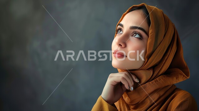 إيماءات التأمل والتمعن, امرأة سعودية تنظر إلى شيء ما بتعابير الاندماج و الحيرة, بورتريه لإمرأة عربية سعودية خليجية محجبة تضع يدها تحت رأسها وتفكر, شرود الذهن في موضوع معين، إيجاد الحلول لمشكلة ما، خلفية رمادي