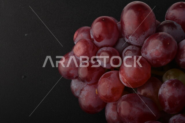 صورة لفاكهة العنب الأرجواني اللذيذ مصورة على خلفية سوداء ، فاكهة العنب الصحية اللذيذة تظهر على شكل عناقيد ، فاكهة صيفية
