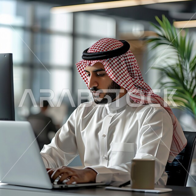 مهن ووظائف سعودية، استخدام الاجهزة التقنية الحديثة، ادارة مهام العمل اليومية في مقر الشركة، صورة مقربة لرجل عربي خليجي سعودي يرتدي الزي التقليدي يجلس في مكتبه يعمل على جهاز الحاسوب المحمول 