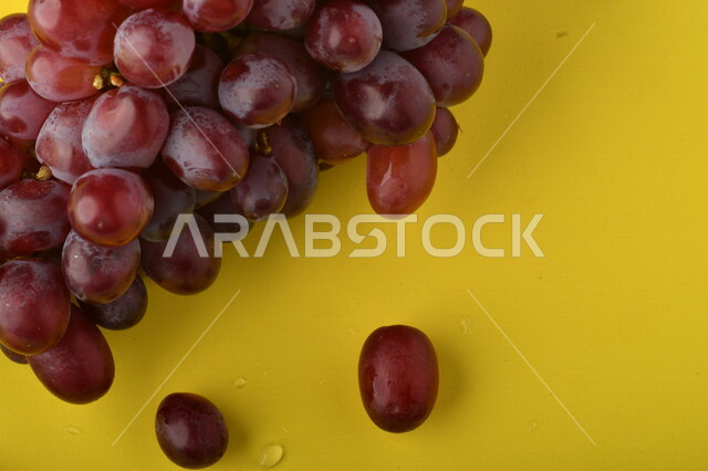 صورة لفاكهة العنب الأرجواني اللذيذ على خلفية صفراء ، فاكهة العنب الصحية اللذيذة تظهر على شكل عناقيد ، فاكهة صيفية