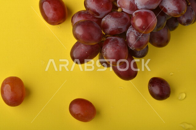 صورة لفاكهة العنب الأرجواني اللذيذ على خلفية صفراء ، فاكهة العنب الصحية اللذيذة تظهر على شكل عناقيد ، فاكهة صيفية