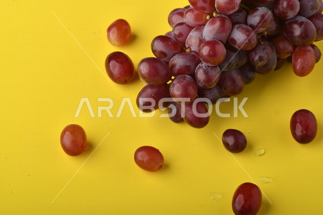 صورة لفاكهة العنب الأرجواني اللذيذ على خلفية صفراء ، فاكهة العنب الصحية اللذيذة تظهر على شكل عناقيد ، فاكهة صيفية