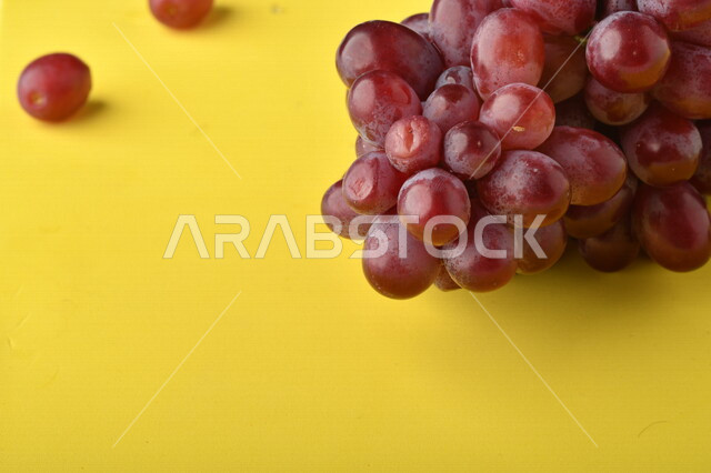 صورة لفاكهة العنب الأرجواني اللذيذ على خلفية صفراء ، فاكهة العنب الصحية اللذيذة تظهر على شكل عناقيد ، فاكهة صيفية