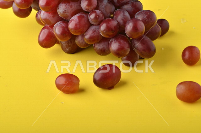 صورة لفاكهة العنب الأرجواني اللذيذ على خلفية صفراء ، فاكهة العنب الصحية اللذيذة تظهر على شكل عناقيد ، فاكهة صيفية