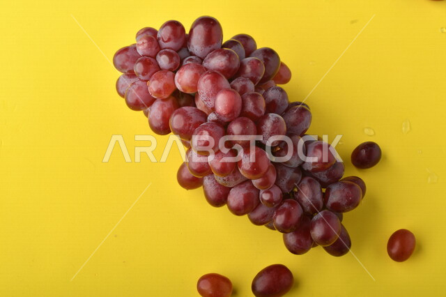 صورة لفاكهة العنب الأرجواني اللذيذ على خلفية صفراء ، فاكهة العنب الصحية اللذيذة تظهر على شكل عناقيد ، فاكهة صيفية