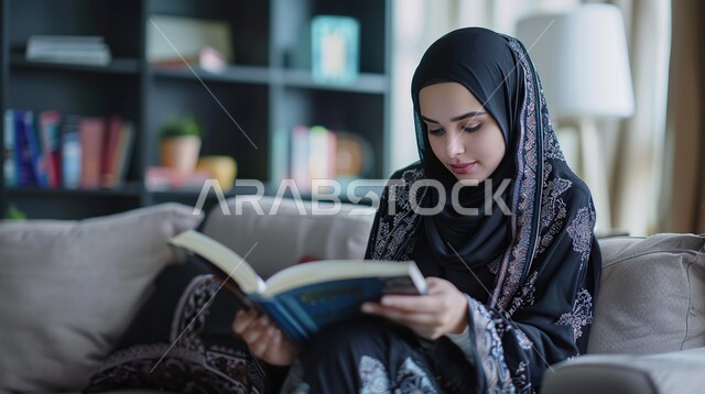 قضاء وقت الفراغ بالتعلم والثقافة، هواية القراءة والاستكشاف، مفهوم التثقيف والبحث العلمي، شابة عربية خليجية سعودية ترتدي العباية والحجاب تجلس على كنبة مريحة تقوم بقراءة كتاب ما
