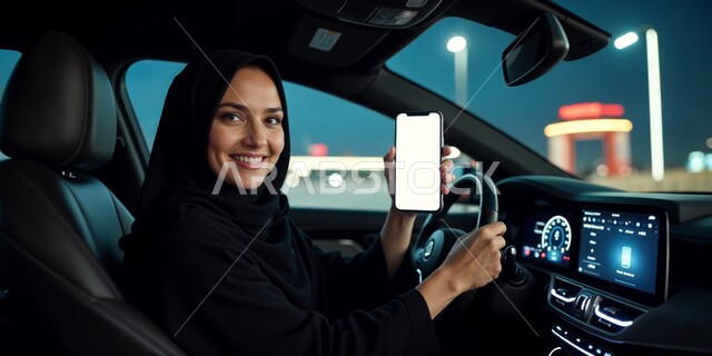 القيادة في الطرقات و الشوارع العامة, استخدام الأجهزة التقنية الحديثة, النظر إلى الكاميرا بإيماءات السعادة و السرور, شابة عربية خليجية سعودية مبتسمة ترتدي العباءة السوداء تجلس داخل السيارة و تمسك بيدها الهاتف المحمول, عرض شاشة بيضاء فارغة عبر الجوال