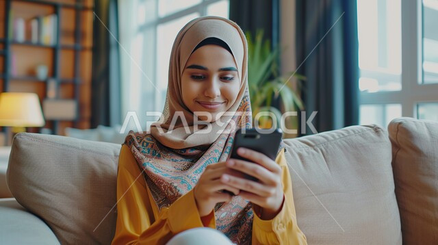 الاستمتاع بقضاء وقت ممتع في إحدى المناطق العامة, تصفح مواقع السوشال ميديا, التواصل عبر التطبيقات الالكترونية الحديثة, صورة مقربة لشابة عربية خليجية سعودية محجبة مبتسمة تقوم بالتحدث مع الأصدقاء عبر الهاتف المحمول