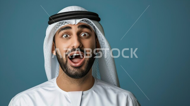 الصدمة والتعجب من حصول أمر ما، ايماءات تدل على الذهول لسماع خبر مفاجئ، بورتريه مقرب لرجل عربي خليجي اماراتي يرتدي الزي التقليدي ينظر إلى الكاميرا بتعابير الدهشة والخوف، خلفية زرقاء