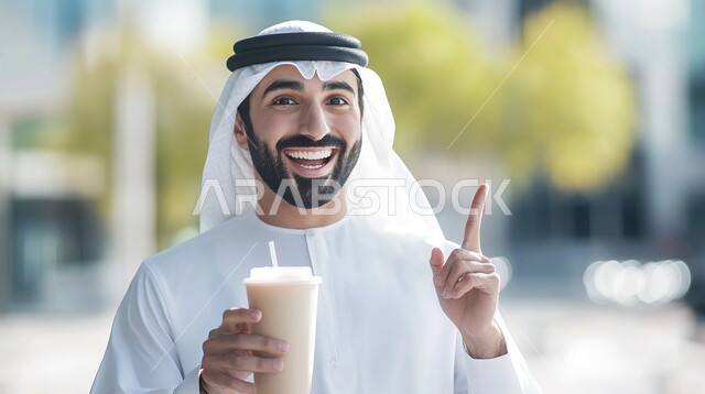 Gestures and expressions of the presence of something, specifying a specific location, signs that specify this place (here), a close-up of a Saudi Arabian Gulf man in traditional dress holding a cup of juice and pointing with his index fingers at something, looking at the camera with gestures of pleasure