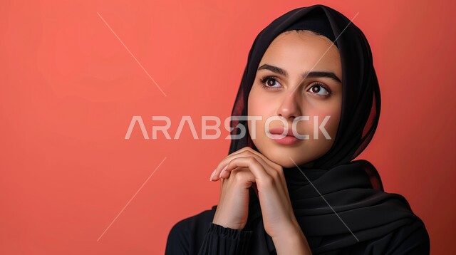 أزياء محجبات عصرية وأنيقة، مفهوم الأنوثة والنعومة، الاهتمام بالمظهر الخارجي، الملامح العربية القوية، بورتريه مقرب لامرأة عربية خليجية سعودية ترتدي الحجاب تضع يدها على ذقنها بإيماءات التفكير، شرود الذهن والنظر الى شيء ما ، خلفية وردية