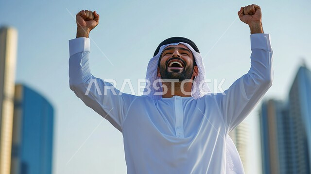 النجاح والقوة وتحقيق الاهداف، إيماءات يدين تدل على الحماس والشغف، صورة مقربة لرجل عربي خليجي سعودي يرتدي الزي التقليدي يرفع يديه للأعلى، المنافسة والتحدي والتشجيع، الفرح والسعادة بالفوز والإنتصار، خلفية الأبراج