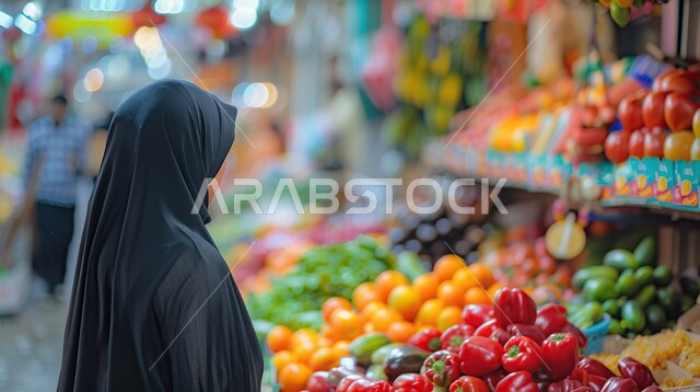 شراء احتياجات المنزل من قسم الخضار والفواكه في المحلات، صورة مقربة لظهر امرأة خليجية سعودية محجبة تنظر للفاكهة الطازجة، قضاء وقت ممتع في التسوق في الأسواق السعودية واختيار الوجبات الخفيفة والأطعمة الصحية