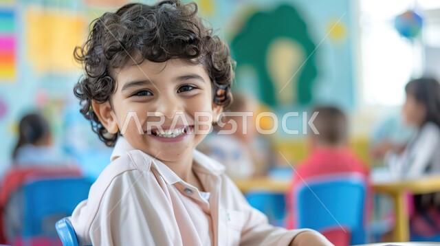 مفهوم التعليم في المملكة العربية السعودية، الحرص على التفوق والنجاح، المتابعة والتركيز على الدروس قي الفصل الدراسي، صورة مقربة لطالب عربي خليجي سعودي يجلس على طاولة الدراسة ينظر إلى الكاميرا بإيماءات السعادة
