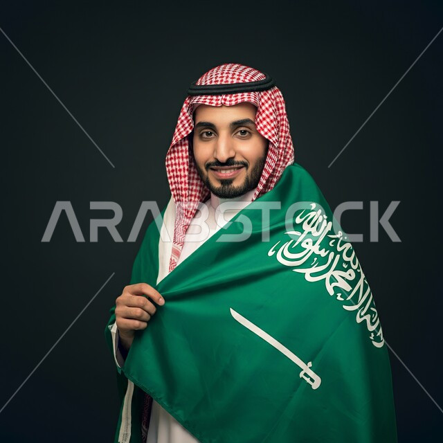 Looking at the camera with gestures of satisfaction and pleasure, a close-up photo of a smiling Saudi Gulf Arab young man wearing a shemagh and a traditional thobe, paying attention to elegance and external appearance.