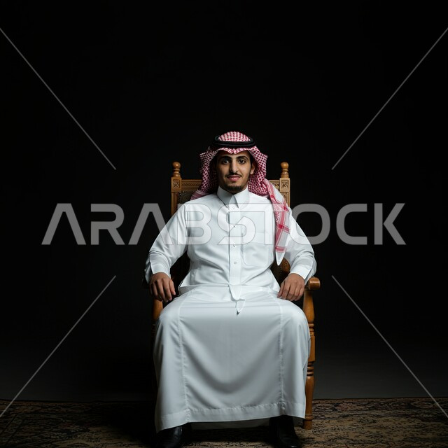 مفهوم الرجولة والأناقة, الاهتمام والعناية بالمظهر الخارجي، الأزياء التراثية العصرية، صورة لرجل عربي خليجي سعودي يرتدي الغترة البيضاء والثوب التقليدي يجلس على كرسي مريح، خلفية سوداء