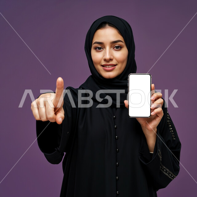 الذكاء الاصطناعي الأجهزة التقنية الحديثة، الاهتمام بالأناقة والمظهر الخارجي، بورتريه مقرب لامرأة عربية خليجية سعودية مبتسمة محجبة ترتدي العباءة السوداء تحمل بيدها الهاتف المحمول و تنظر إلى الكاميرا بإيماءات السعادة و السرور, عرض شاشة بيضاء فارغة عبر الجوال, خلفية زرقاء