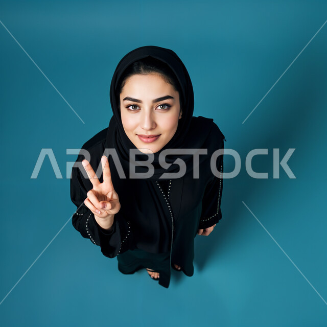 إيماءات الابتسامه السرور والثقه بالنفس ، الذكاء الاصطناعي مفهوم النعومة و الأنوثة، الاهتمام بالأناقة والمظهر الخارجي، صورة مقربة لامرأة عربيه خليجيه سعودية مبتسمة محجبة ترتدي العباءة والحجاب،  أزياء محجبات عصرية حديثة, خلفية زرقاء