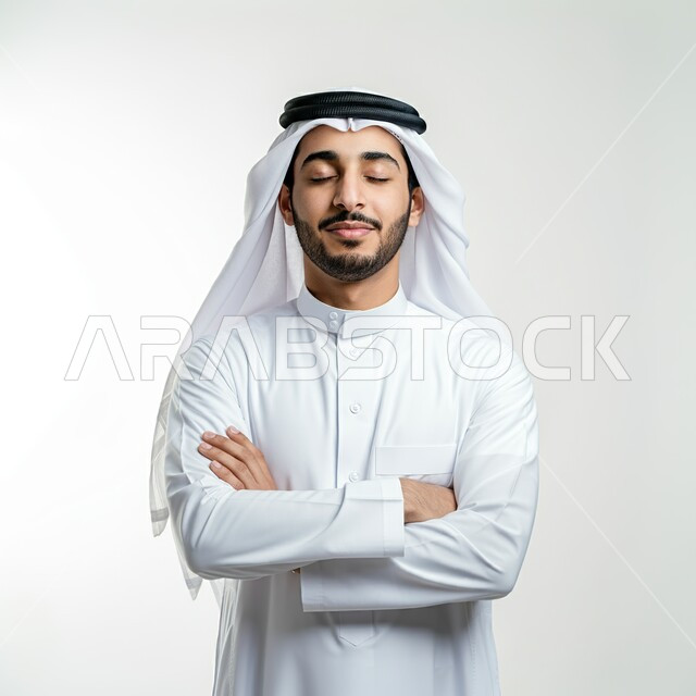 الوقوف بإيماءات ايدي متقاطعة، بورتريه مقرب لرجل عربي خليجي سعودي يرتدي الثوب التقليدي والغترة البيضاء يغمض عينيه بتعابير الاسترخاء، التخيل وتذكر شيء ما، الاهتمام بالاناقة والمظهر الخارجي، خلفية بيضاء
